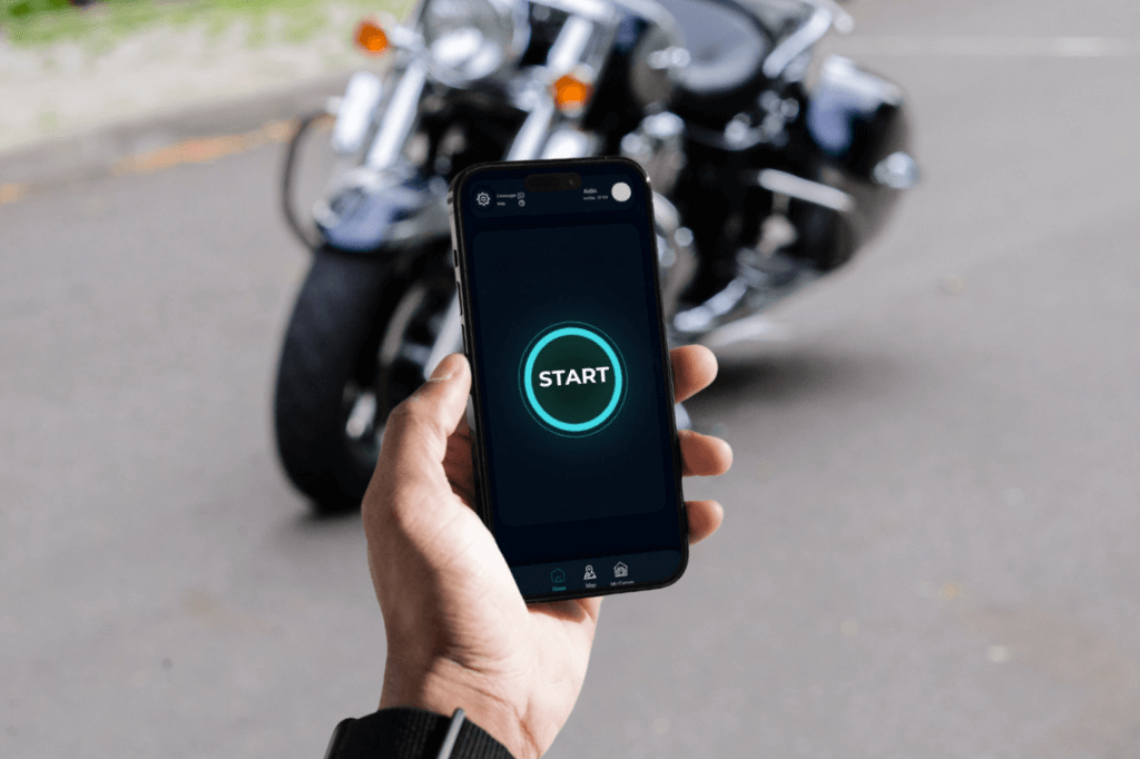 Hand holding a phone displaying a start button, with a motorcycle visible in the distance