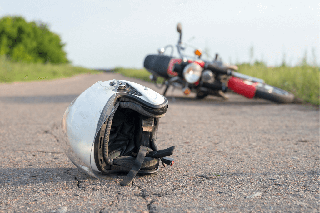 Motorcycle helmet on the road, with a motorcycle lying on its side in the distance