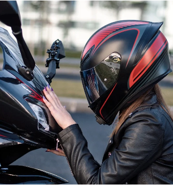 Woman in a motorcycle helmet kneeling in front of a motorcycle, hand resting on the front.