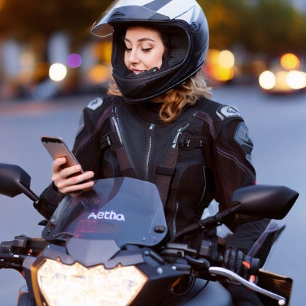 Woman sitting on a parked motorcycle, looking at her cell phone