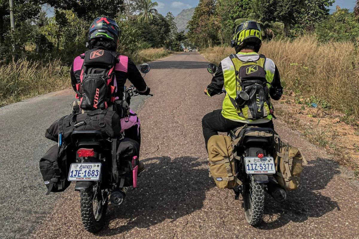 View from behind of two people riding motorcycles down an Asian back road.